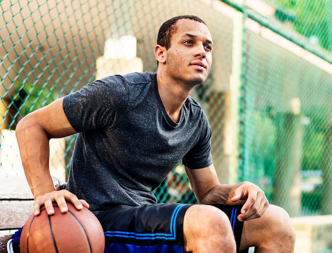 Teen boy sitting with basketball represents finding answers to FAQs on how AKLIEF® Cream works to treat teenage acne