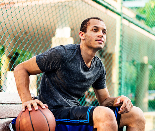 Teen boy sitting with basketball represents finding answers to FAQs on how AKLIEF® Cream works to treat teenage acne