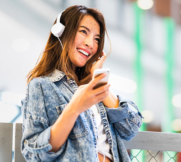 Smiling teen girl with headphones holding cell represents finding answers to FAQs on how AKLIEF® Cream works to treat acne